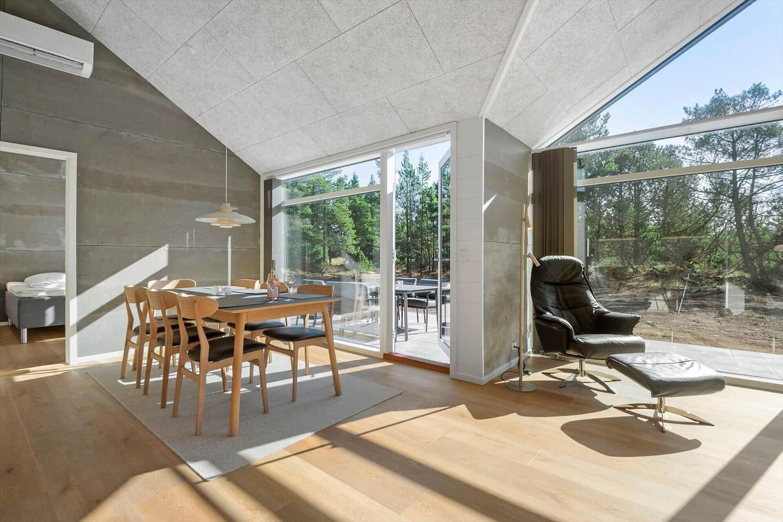 Dining area with wooden table and chairs. Large windows with forest view. Leather armchair and ottoman.