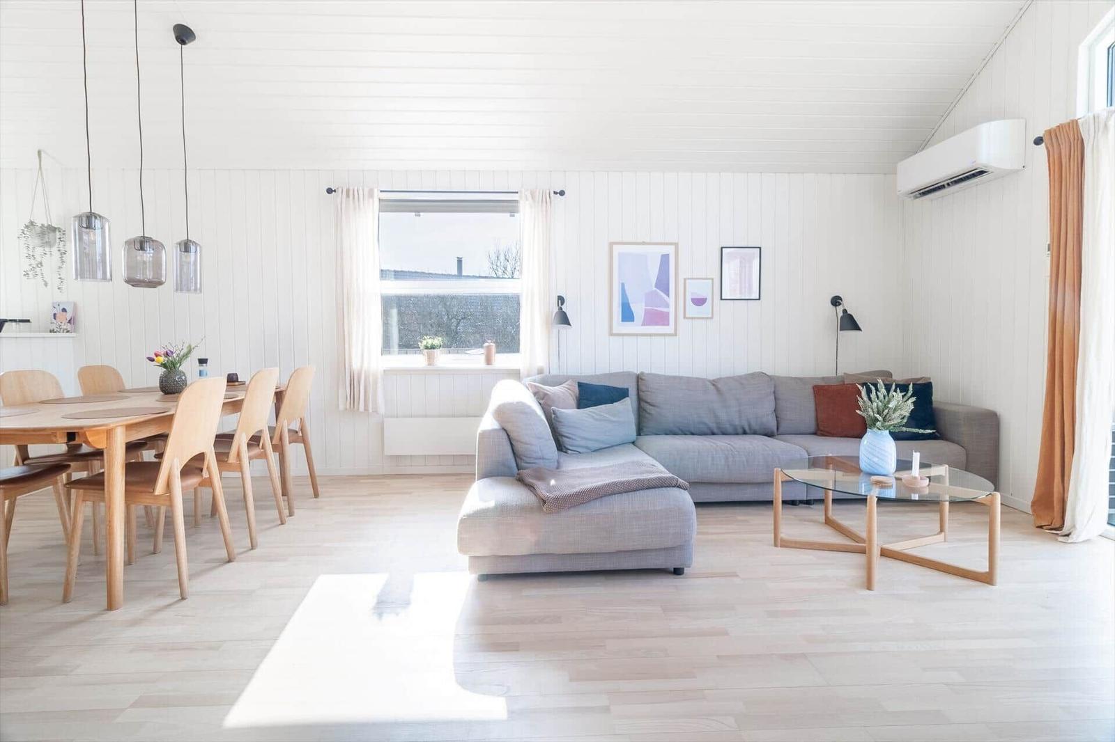 Wohn- und Essbereich mit Sofa, Tisch und Stühlen. Weiße Wände und Holzboden.