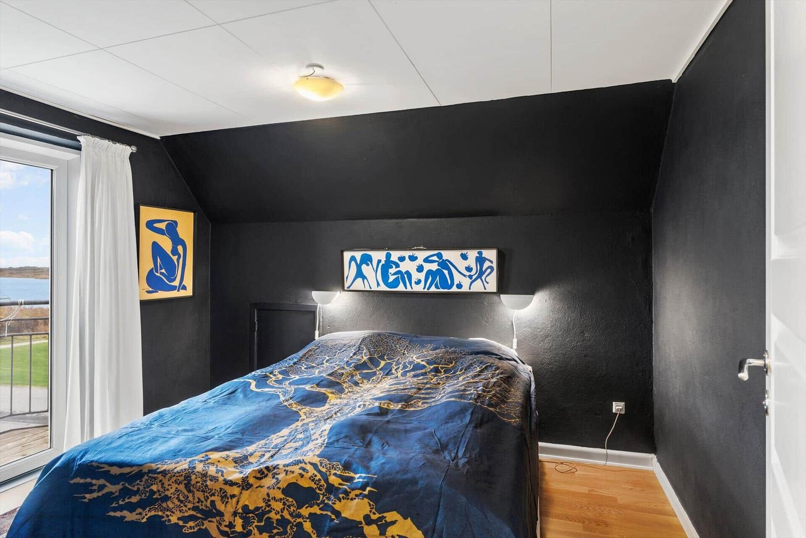 Schlafzimmer mit Bett, schwarzen Wänden und Fenster zum See.