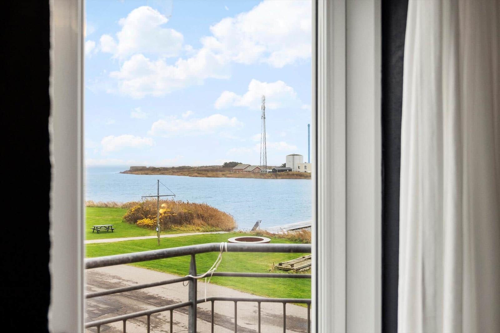 Blick vom Balkon auf Wasser, Grünfläche und entfernte Gebäude.