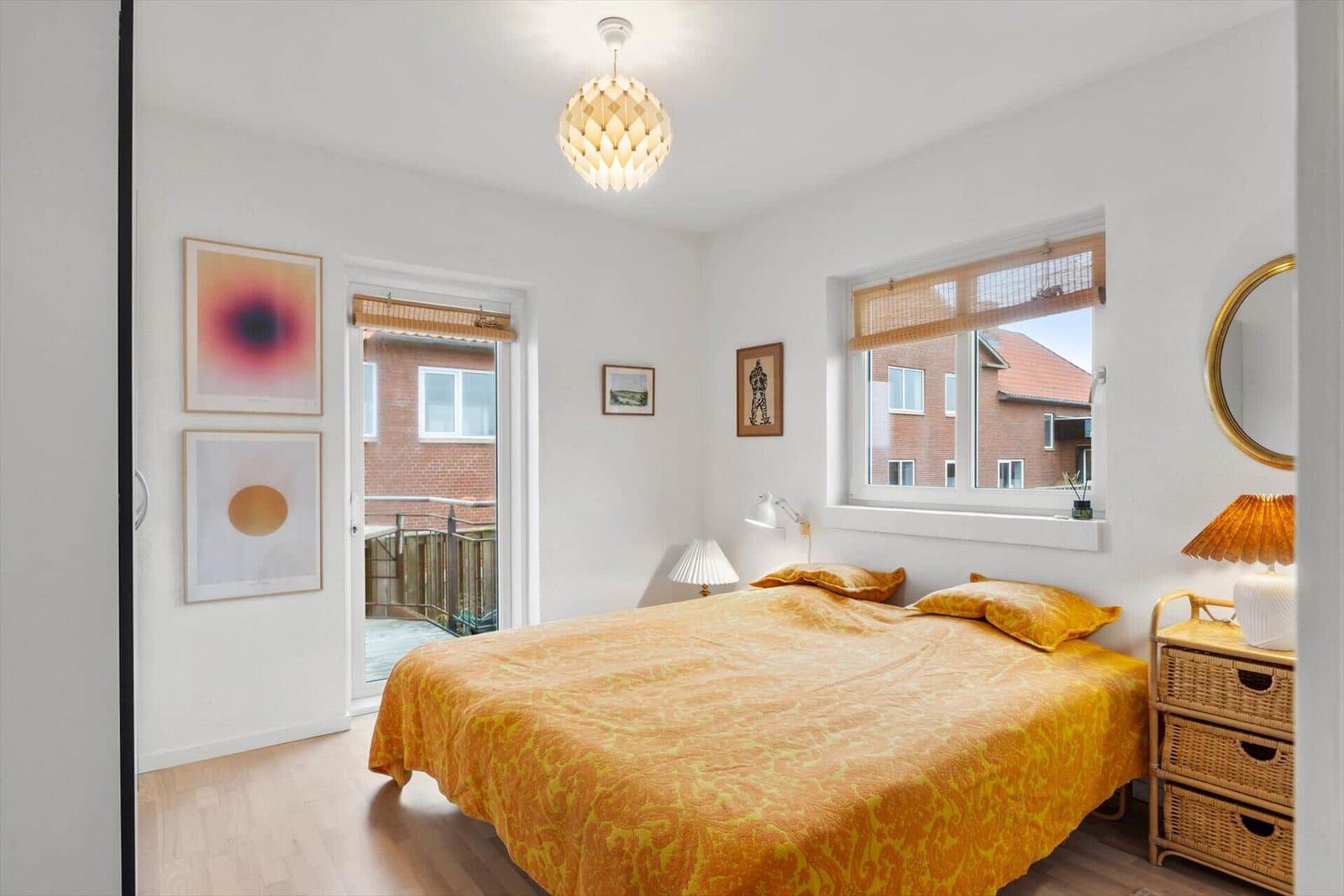 Schlafzimmer mit Bett, Fenster und Balkontür. Wandbilder und Lampen.