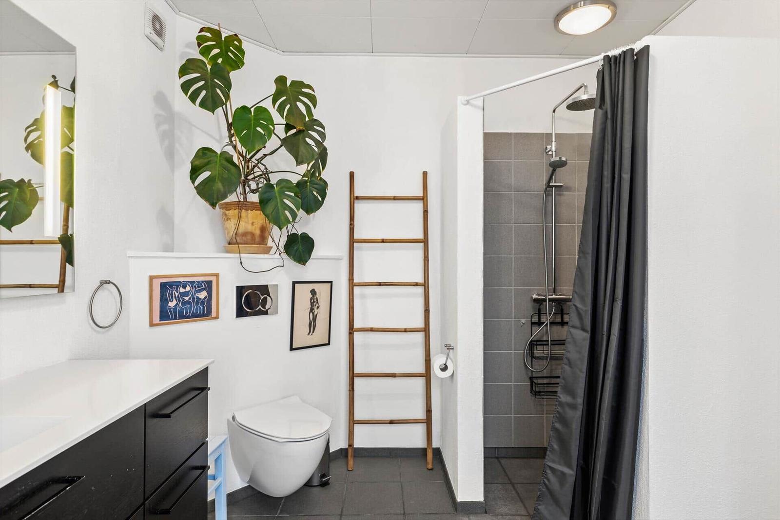 Badezimmer mit Dusche, Toilette, Waschtisch und Pflanze.