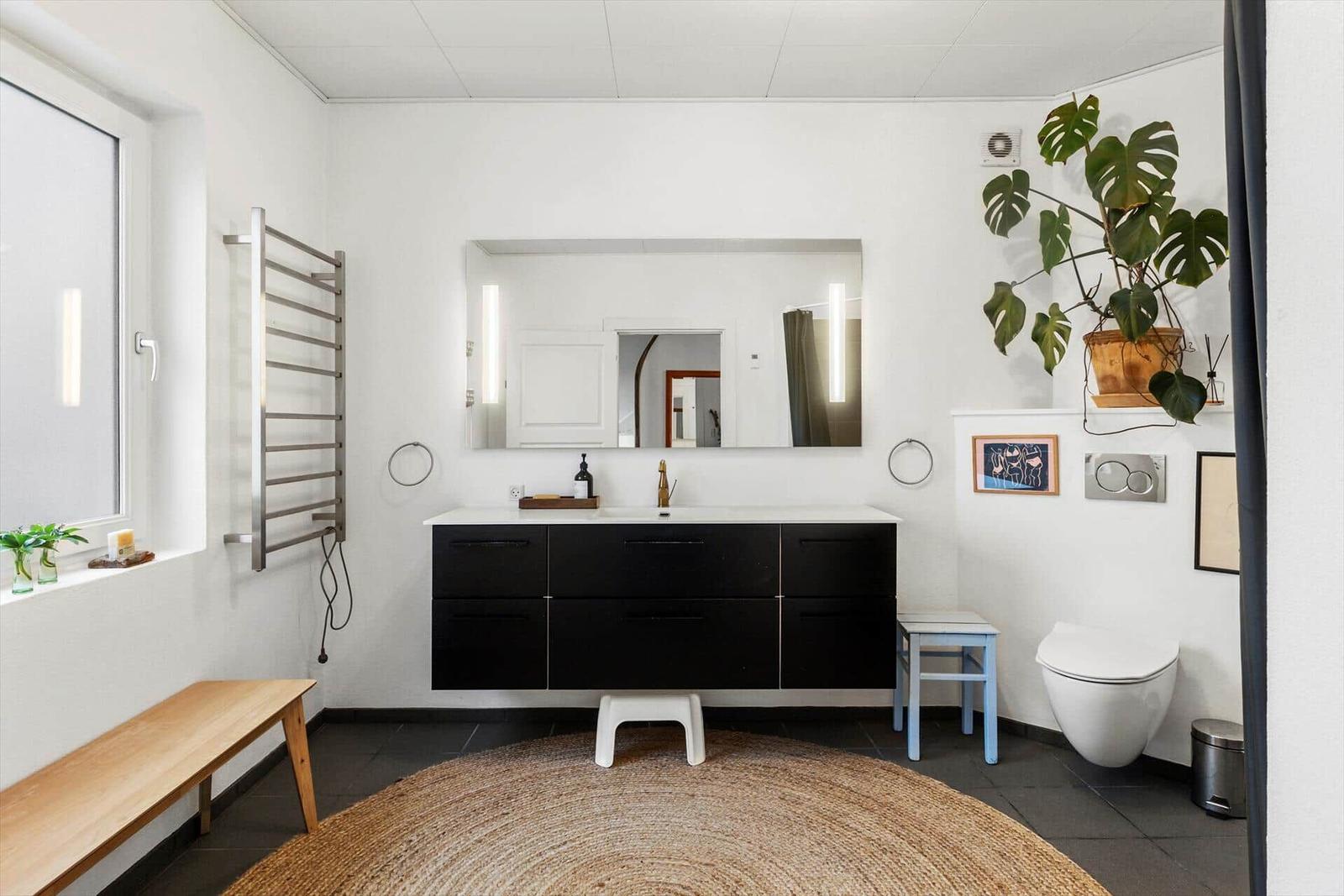 Badezimmer mit Waschbecken, Spiegel, Toilette und Pflanze.