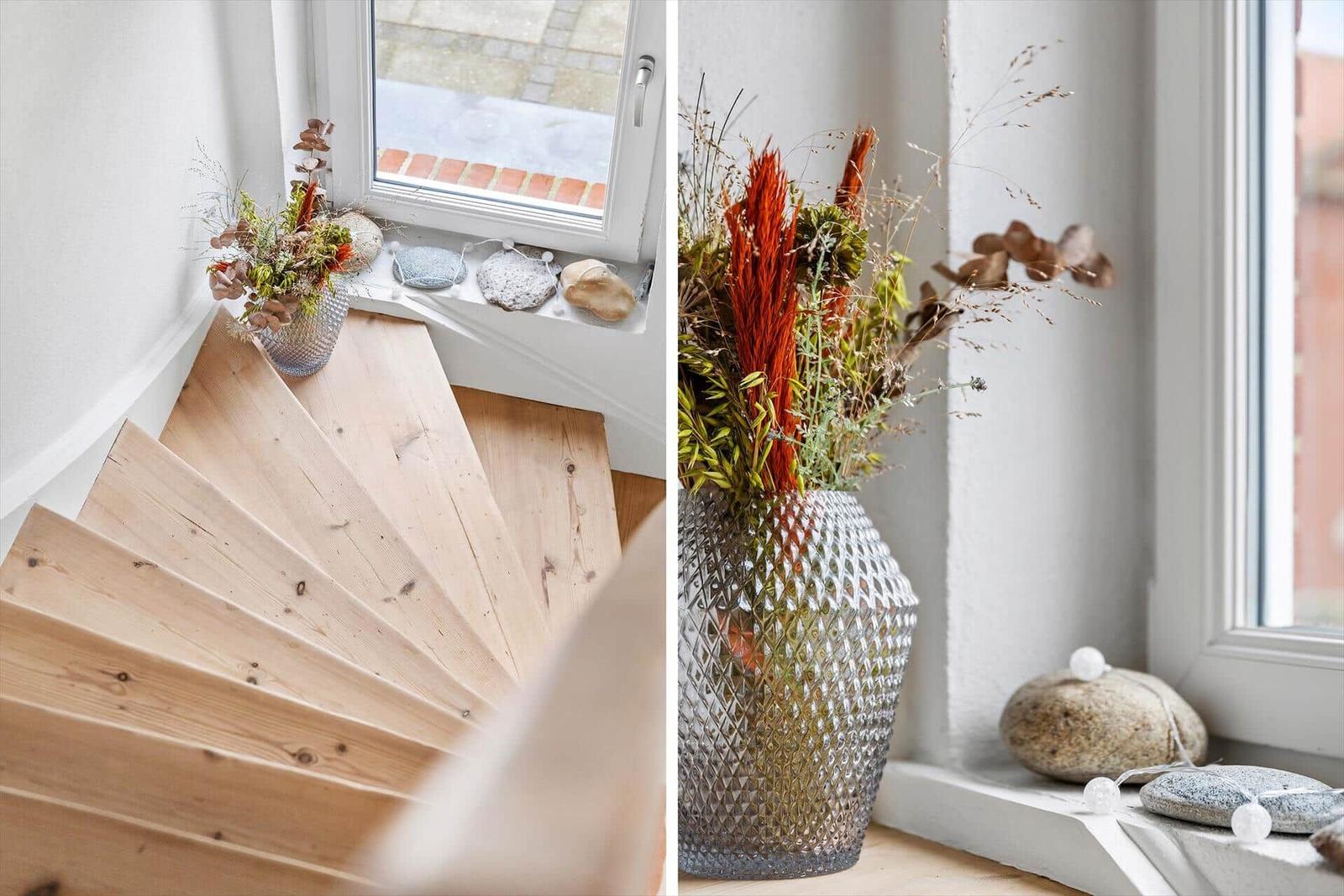 Holztreppenbereich mit Blumenarrangement am Fenster.