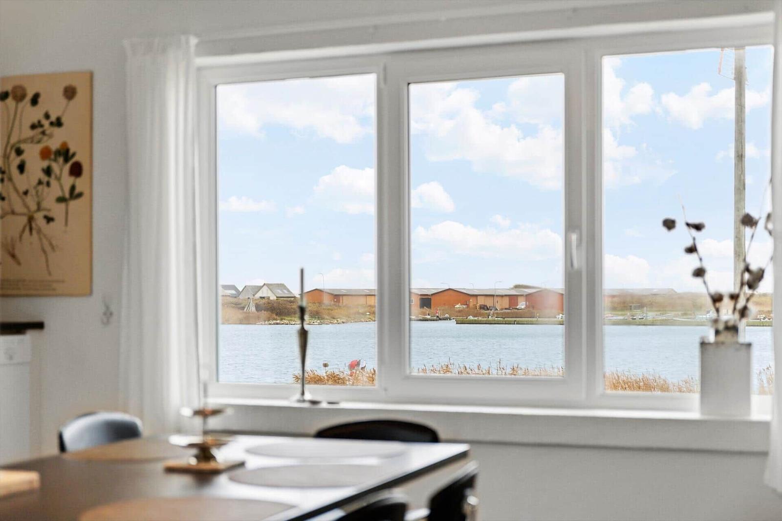 Großes Fenster mit Blick auf Wasser und Häuser. Tisch und Stühle im Vordergrund.