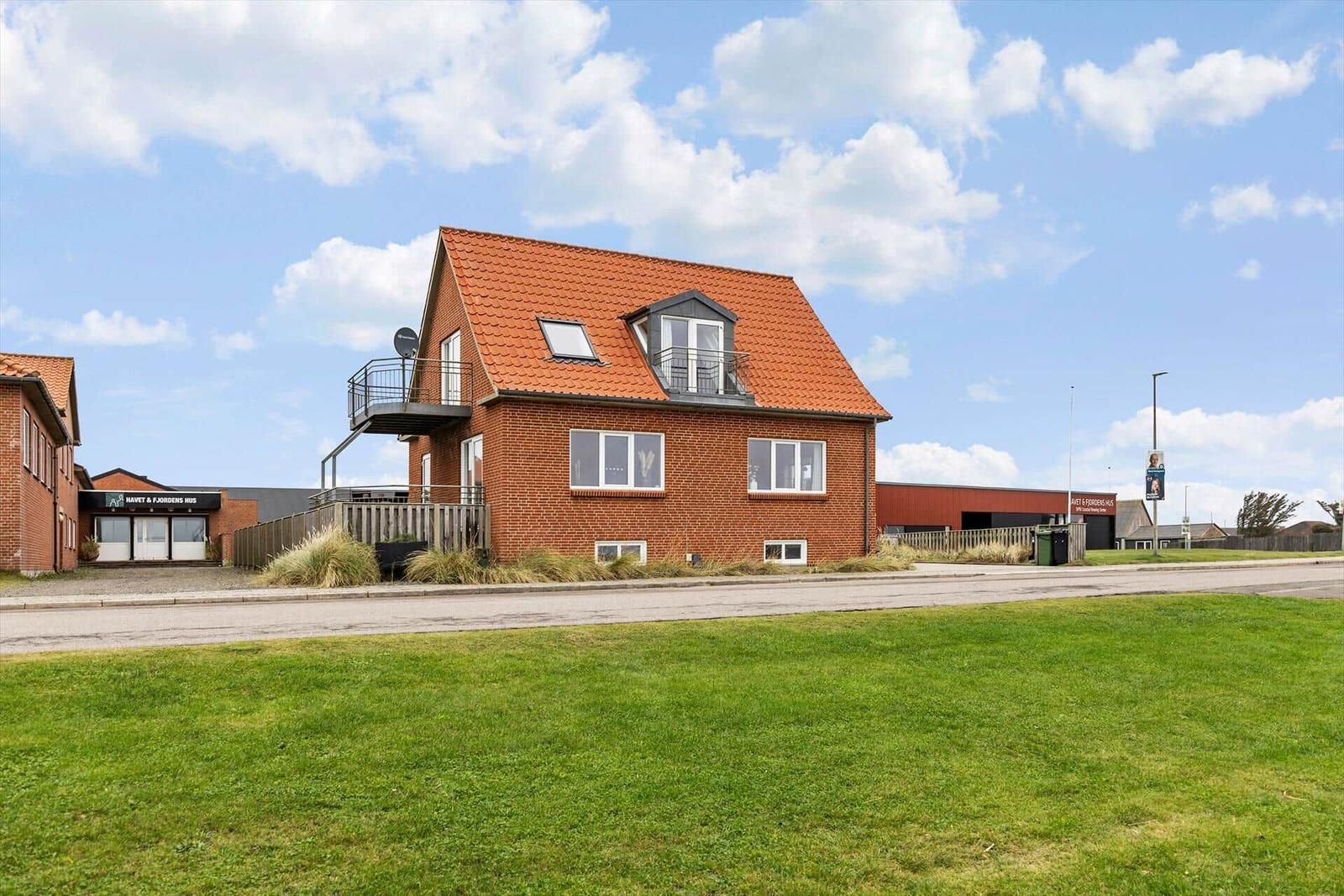 Ein zweistöckiges Haus mit rotem Dach und Balkon. Grasfläche vorne.