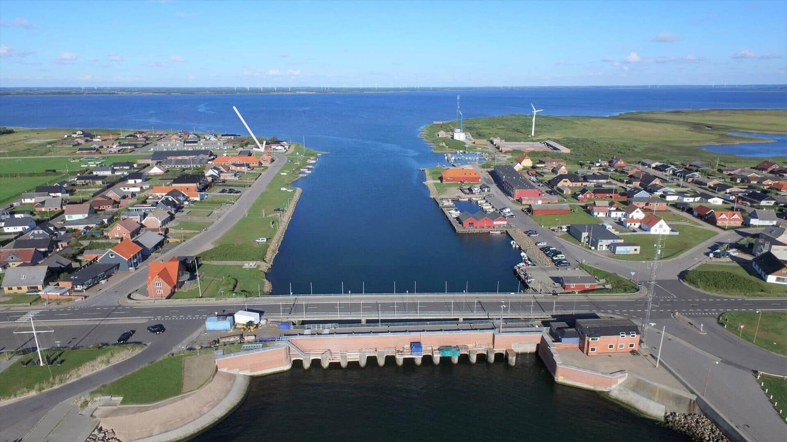 Aerial view of a coastal village with harbor, bridge, and wind turbines.