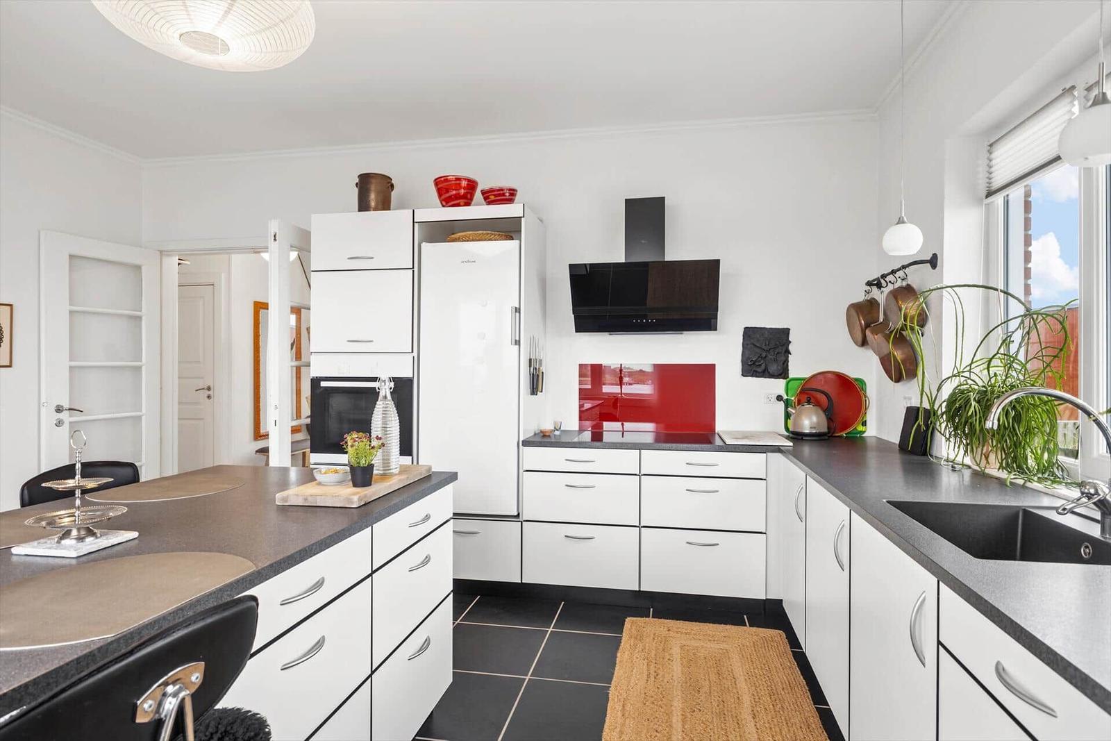 Moderne Küche mit weißen Schränken, schwarzen Arbeitsflächen und rotem Backsplash.