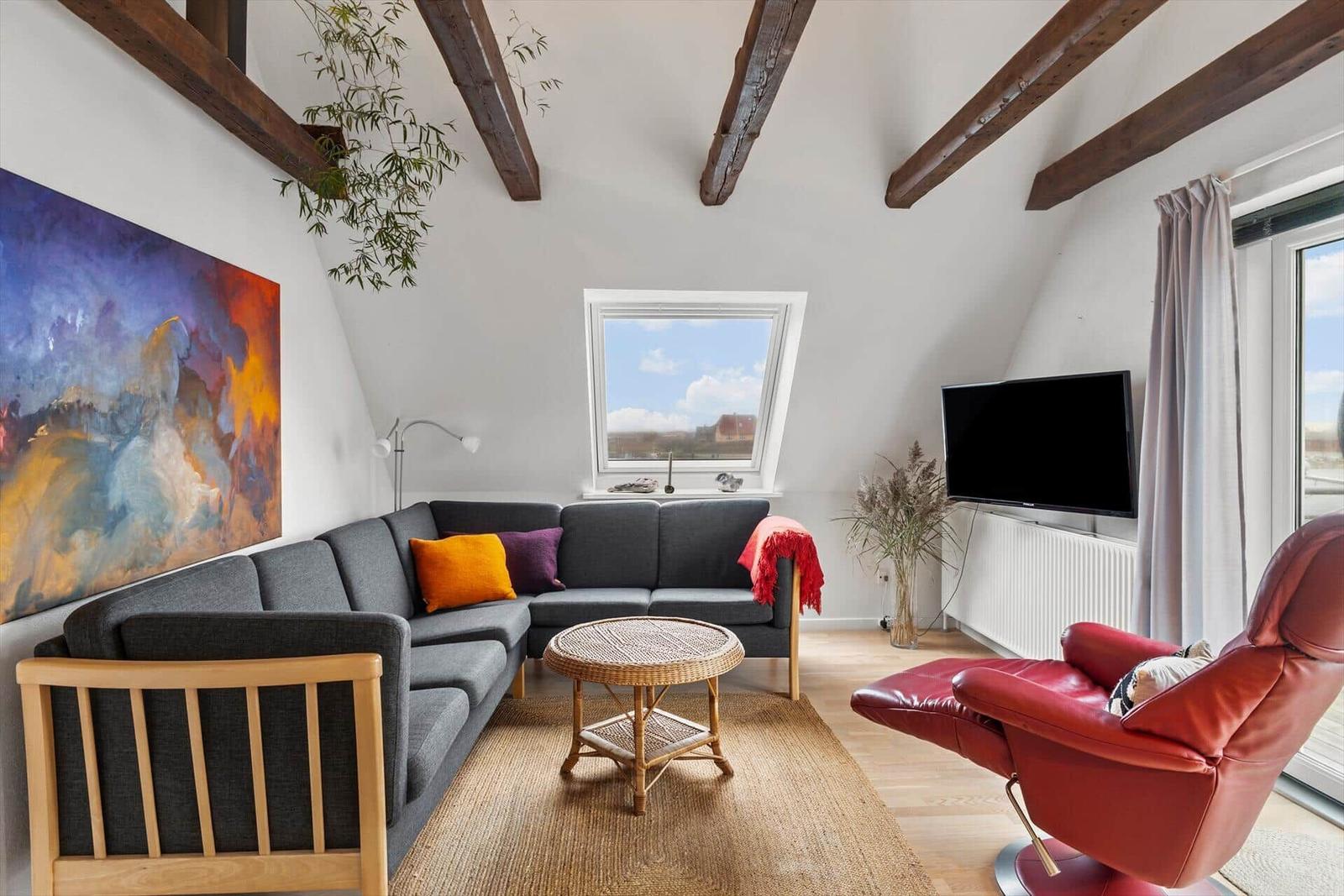 Wohnzimmer mit grauem Sofa, rotem Sessel und Holzbalken an der Decke.