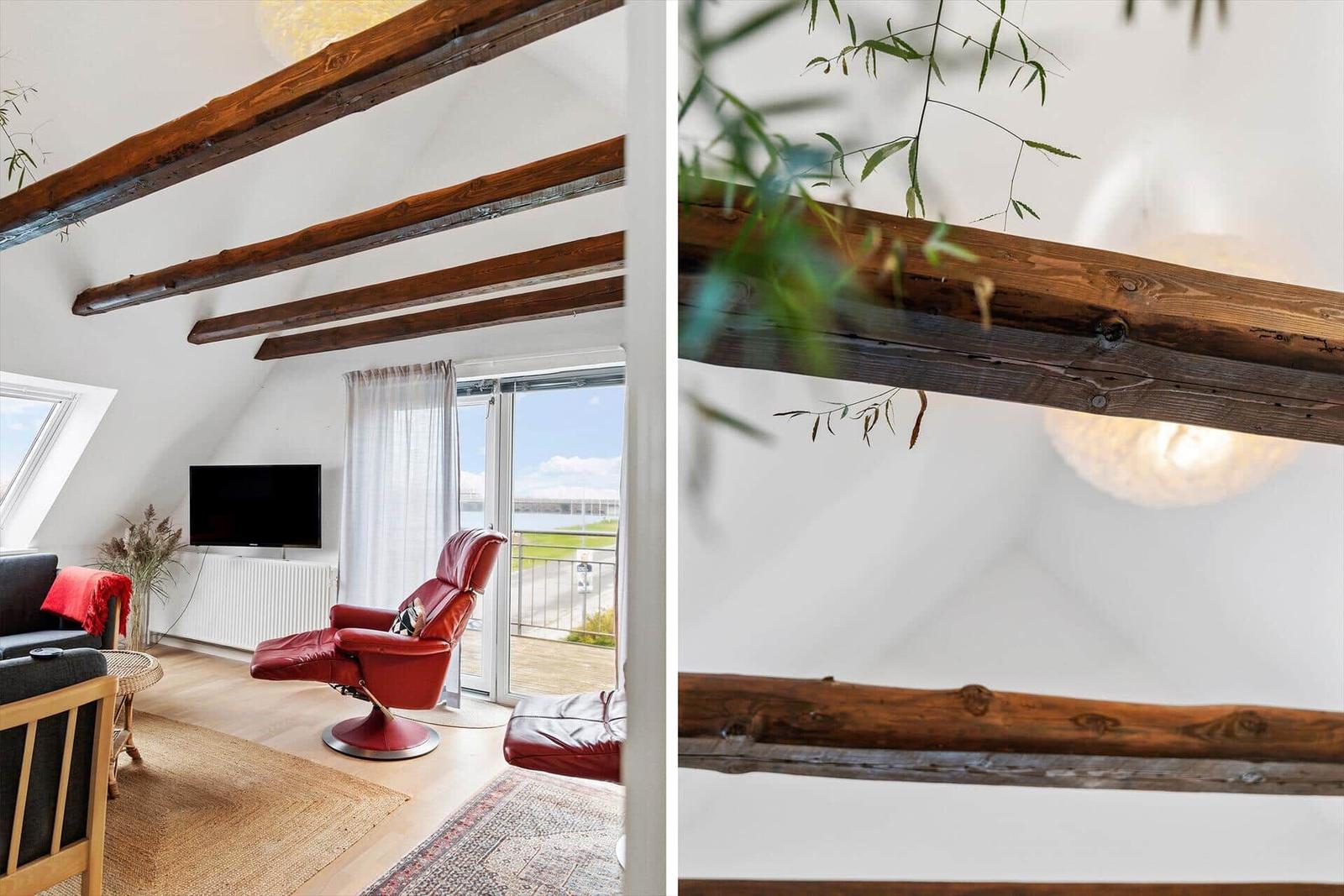 Wohnzimmer mit rotem Sessel, Holzbalken und Blick auf den Außenbereich.