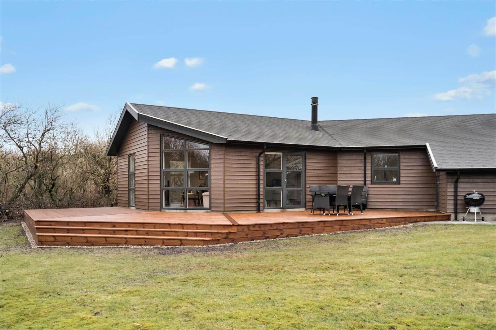 Modern wooden cabin with terrace, grill, and large windows.