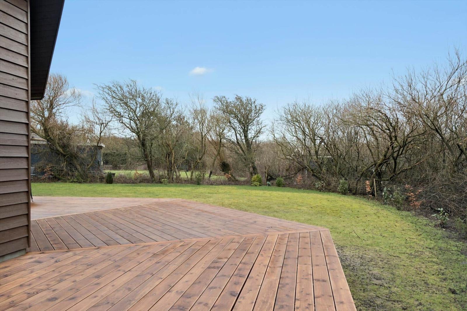 Wooden terrace with view of green lawn and trees in the background.