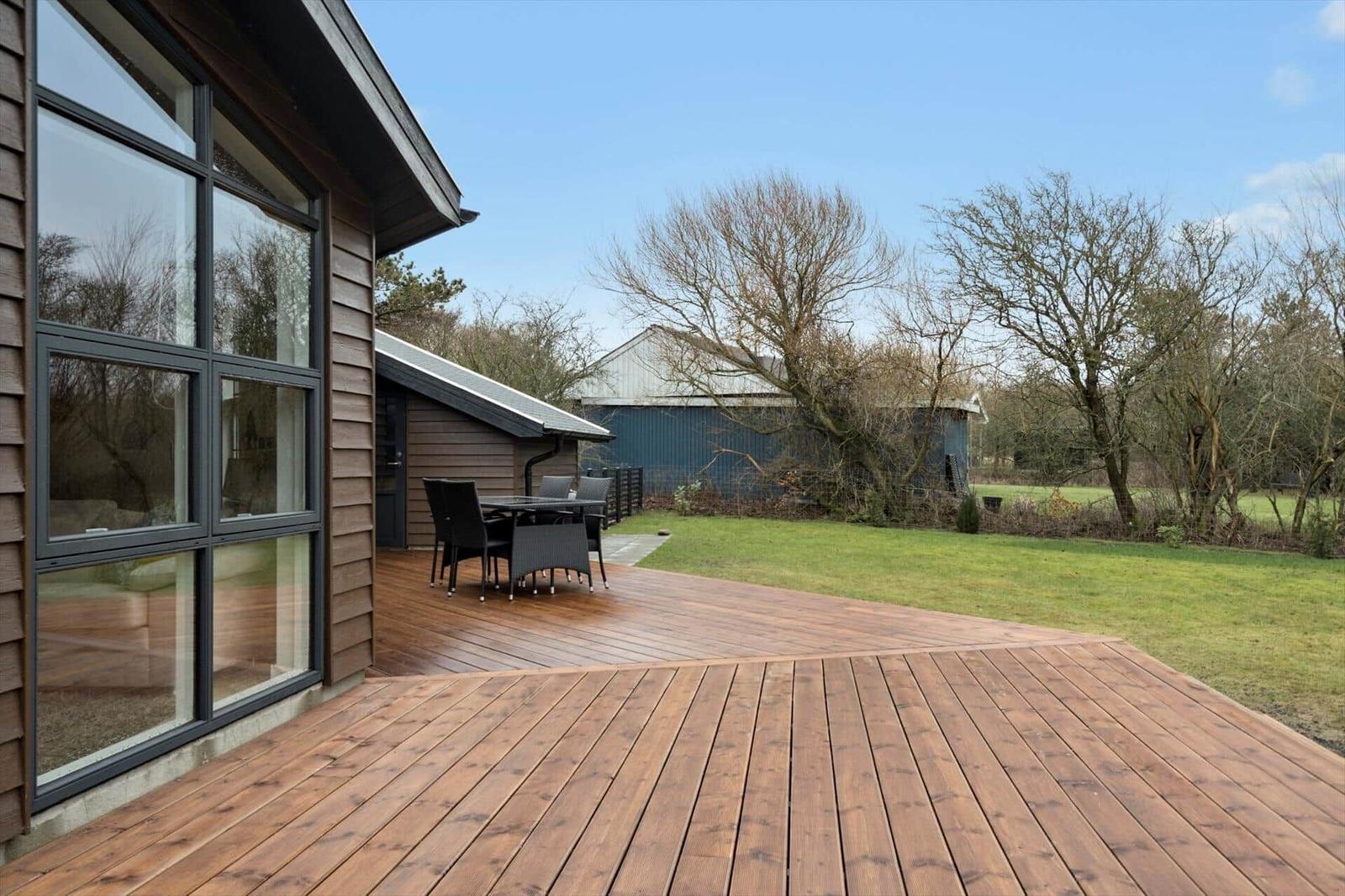 Wooden terrace with seating, view of lawn and farm building.