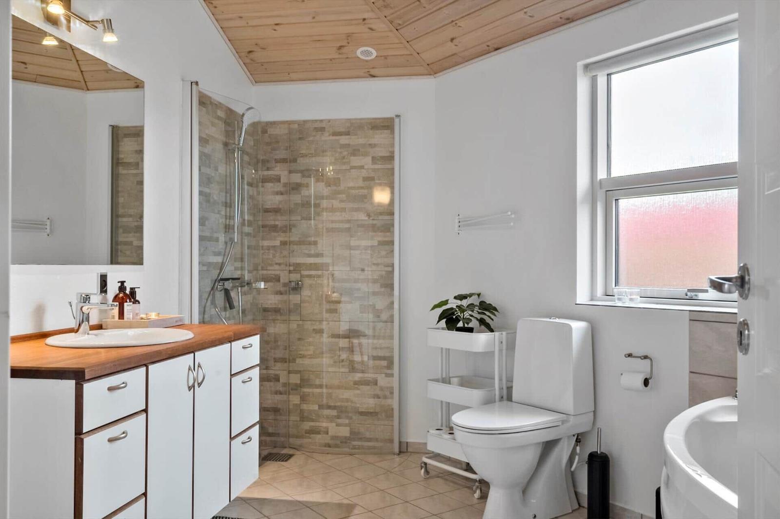 Bathroom with shower, toilet, and sink. Wooden ceiling and window with daylight.
