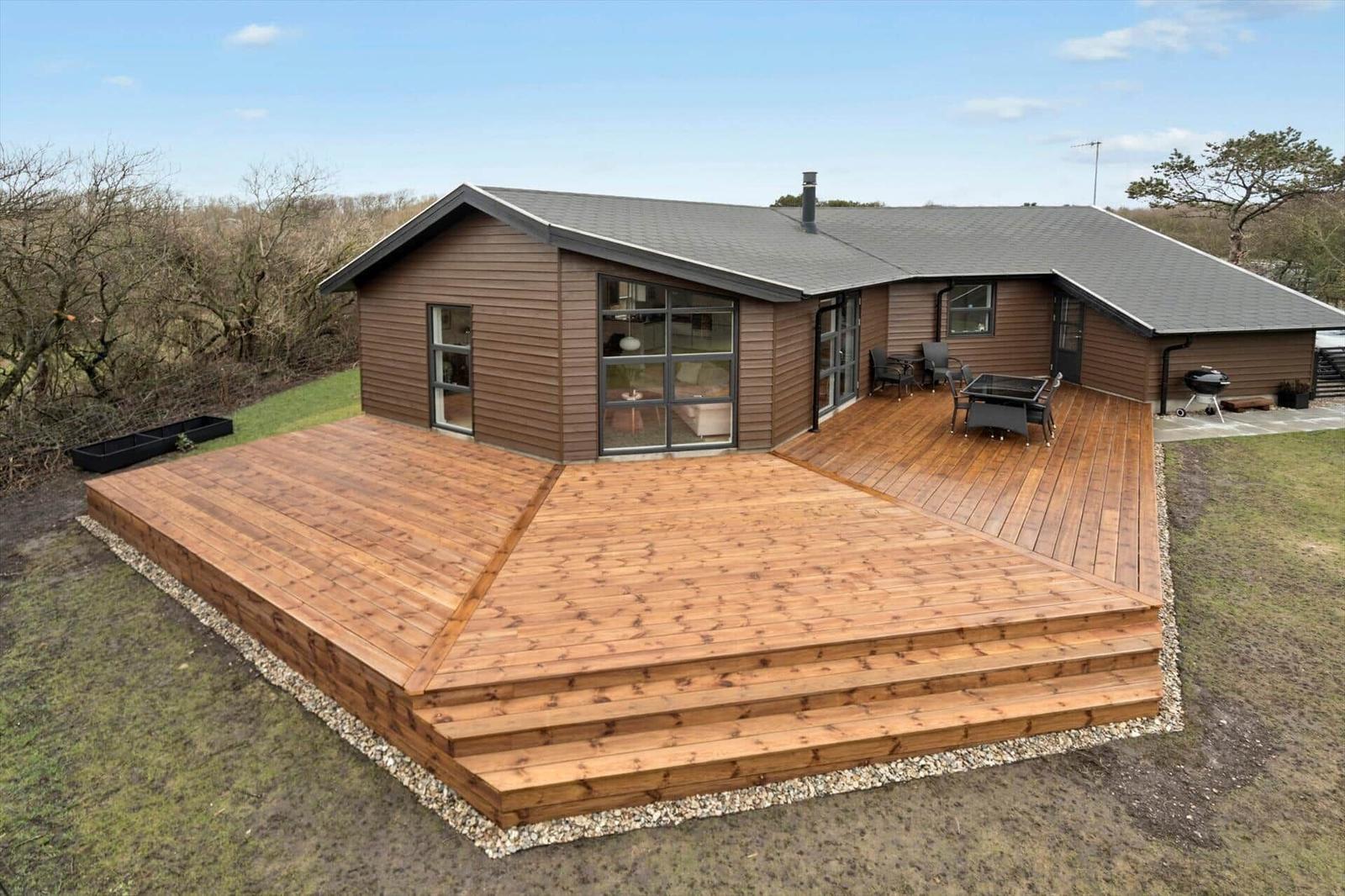 Modern villa with large wooden terrace and outdoor grill area.