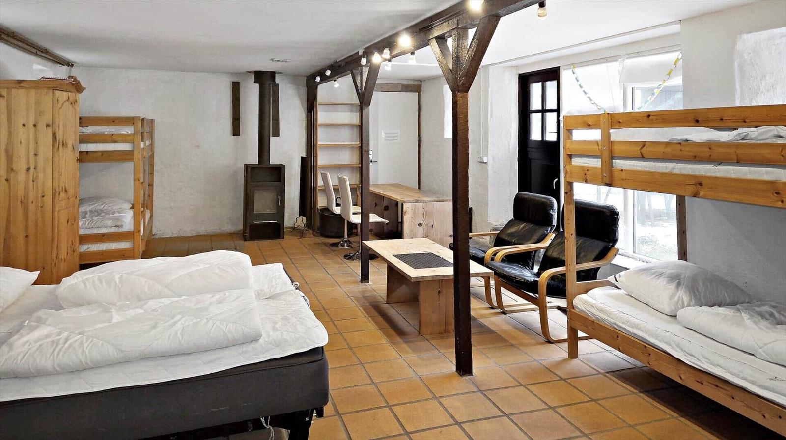 Room with multiple sleeping areas, wooden beds, seating, and wood stove.