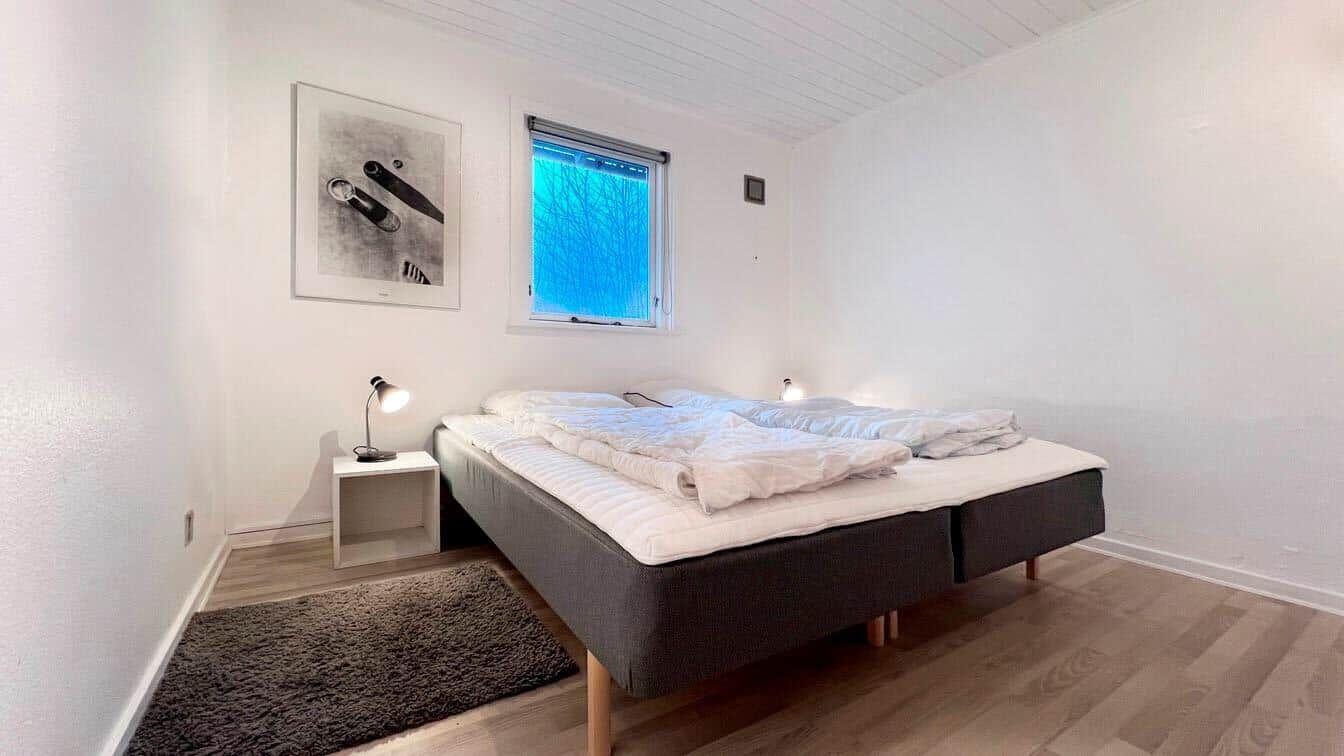 Schlafzimmer mit Bett, Nachttisch und Fenster. Holzboden und Wandbilder.
