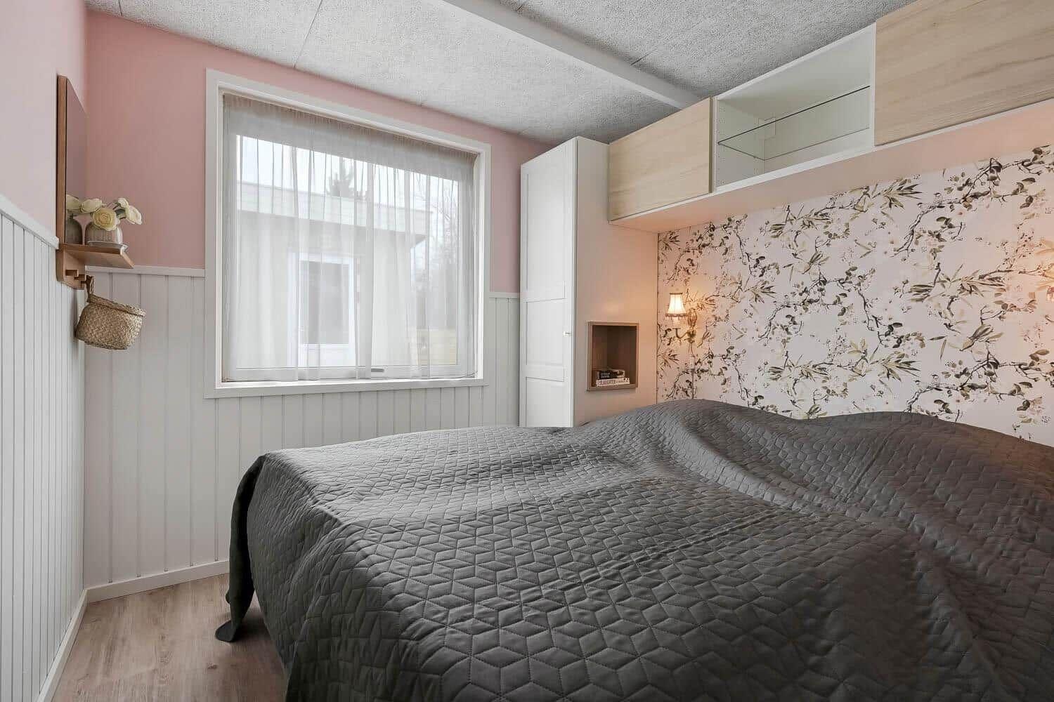 Schlafzimmer mit Bett, Fenster und Wand mit Blumenmuster.