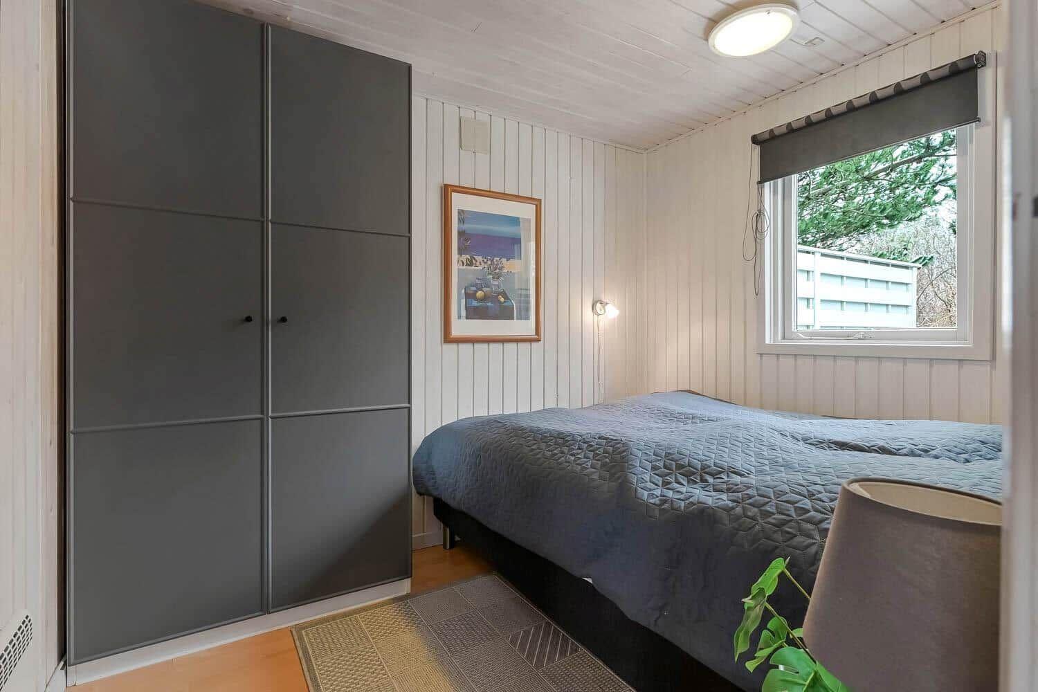 Schlafzimmer mit Bett, Kleiderschrank und Fenster mit Blick auf Außenbereich.