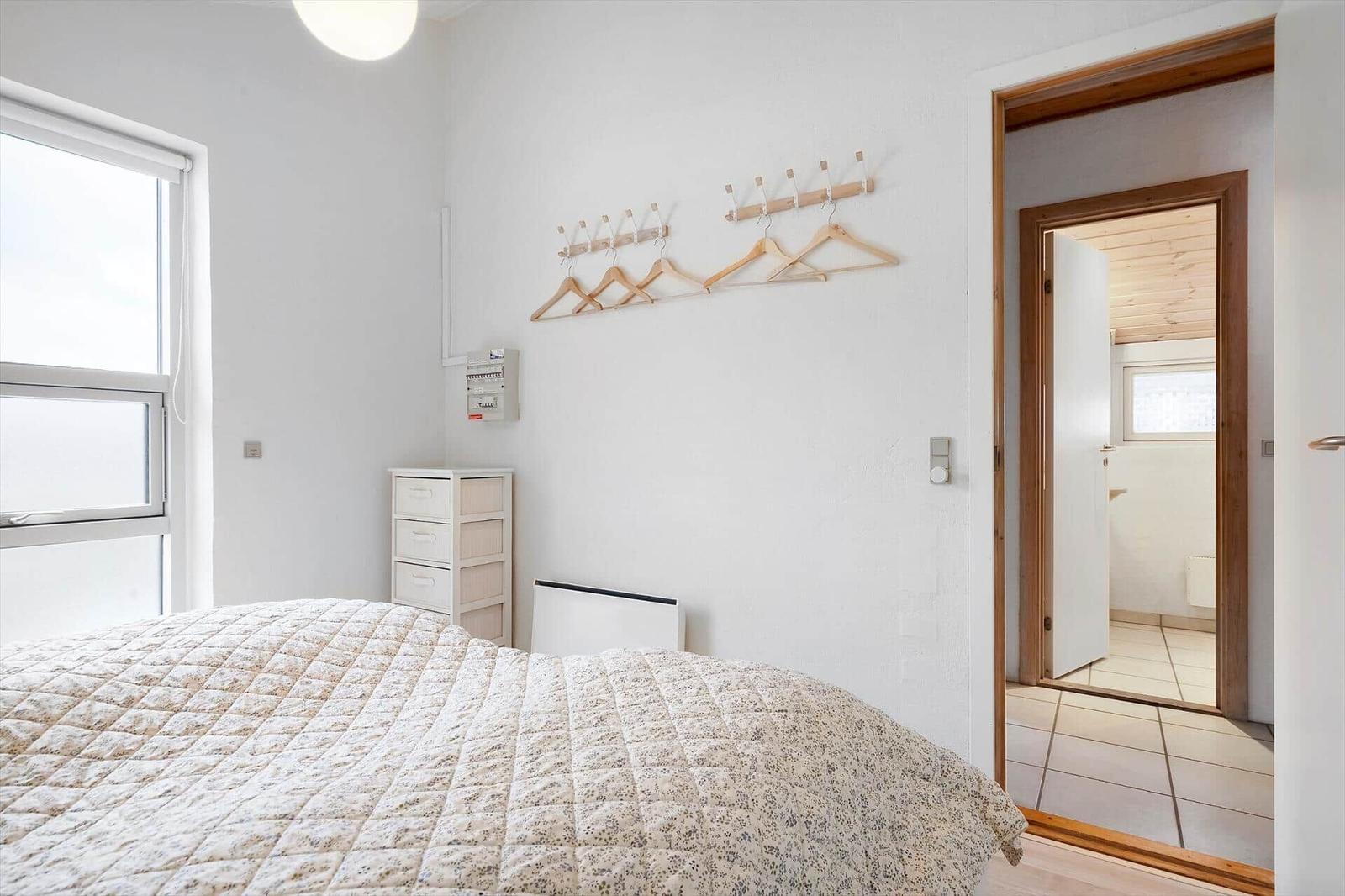 Schlafzimmer mit Bett, Kleiderständer und Fenster. Durchgang zur Badewanne.