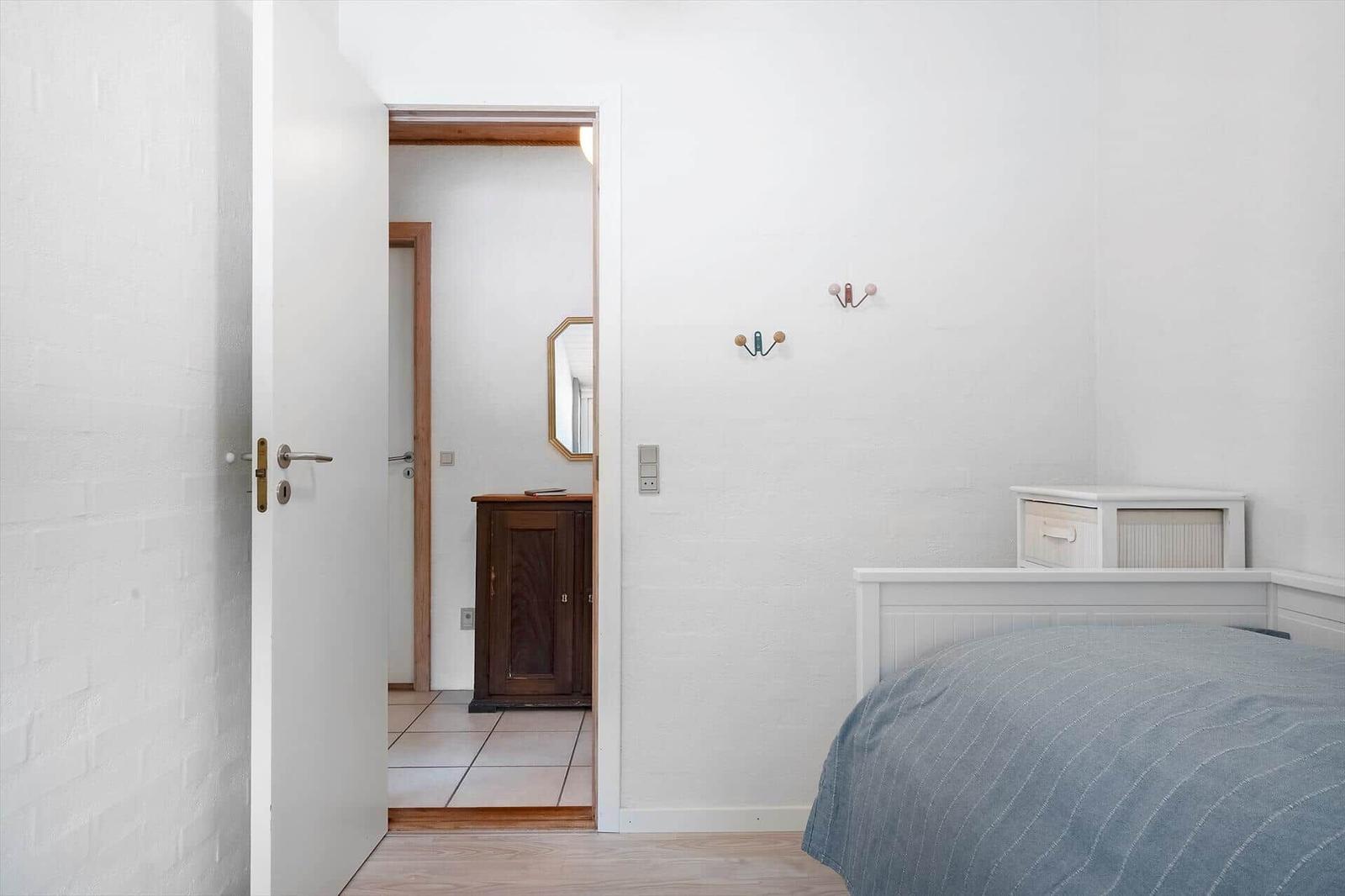 Schlafzimmer mit Bett, Kleiderhaken und Tür zum Flur.