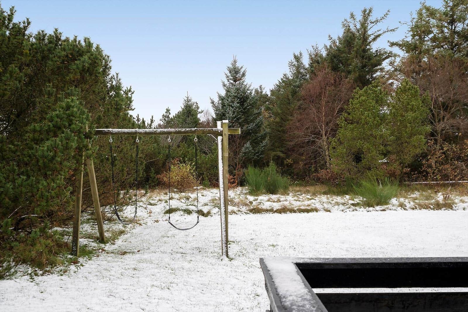 Schneebedeckter Spielplatz mit Schaukel im Wald.