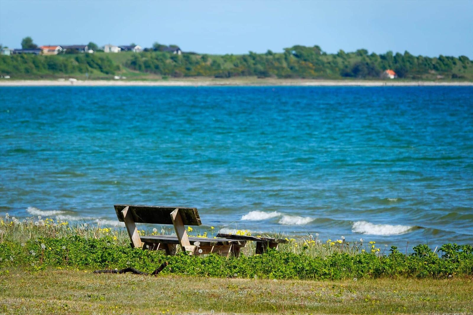 Wooden bench by the shore with view of turquoise water and green hills in the background.