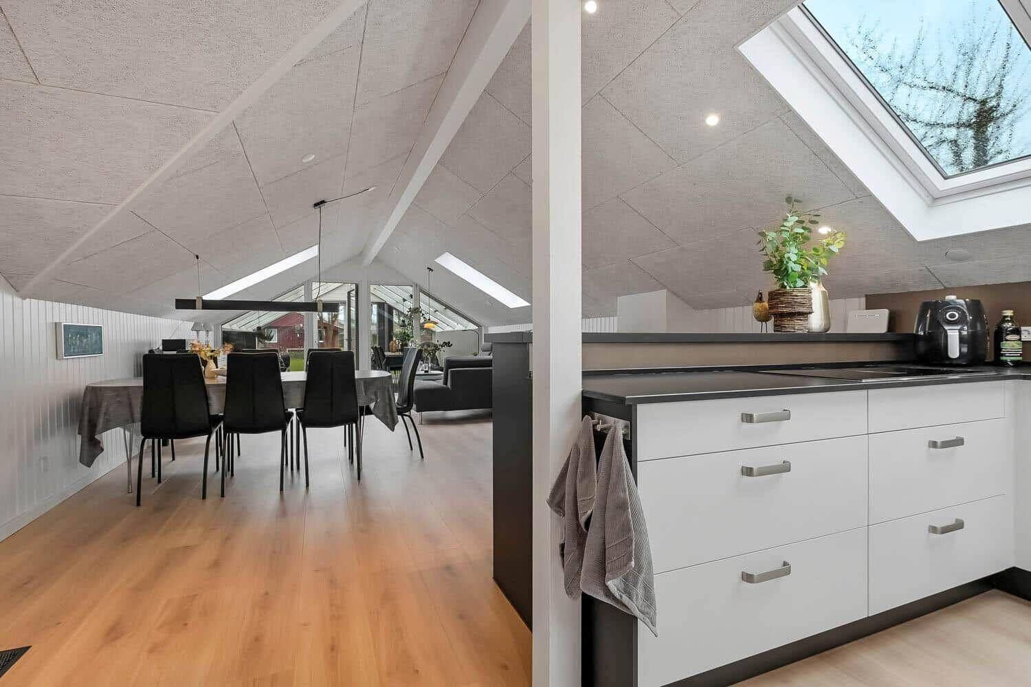 Küche mit Arbeitsfläche und Fenster. Essbereich mit Tisch und Stühlen. Holzboden und Dachschrägen.
