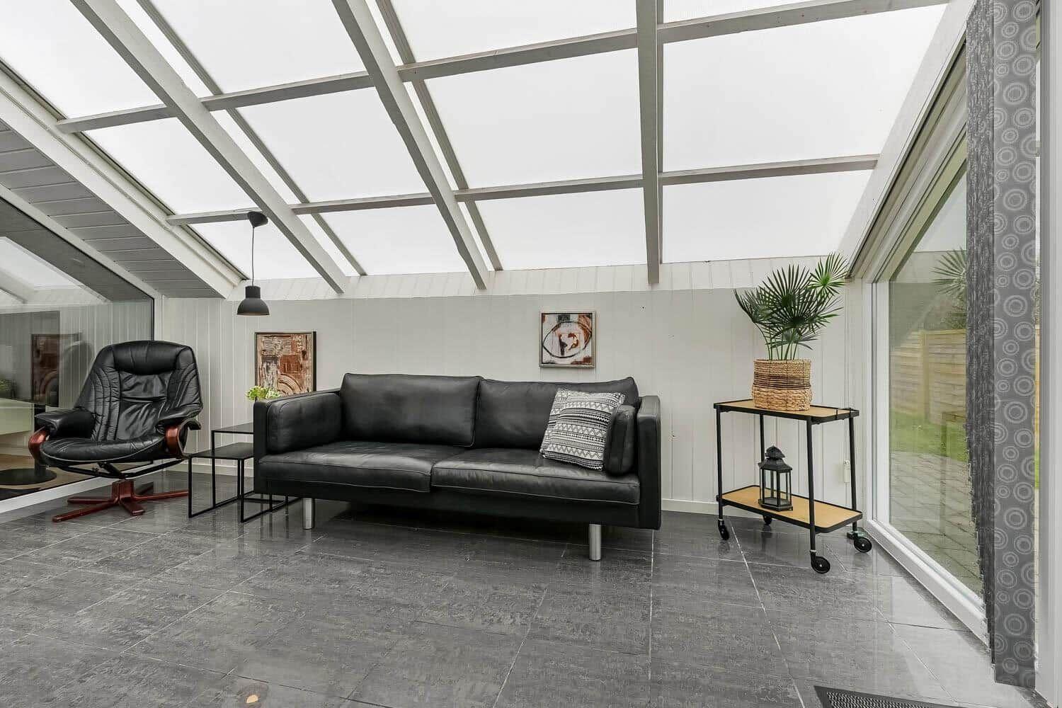 Sofa und Sessel unter Glasdach mit Pflanze und Wandbildern.