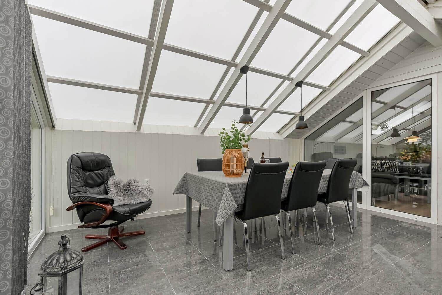 Dining area with table, chairs, and recliner under glass roof.