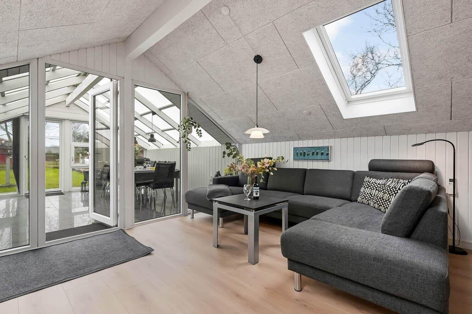 Wohnzimmer mit grauem Sofa, Tisch und Dachfenster. Durchgang zur Terrasse.