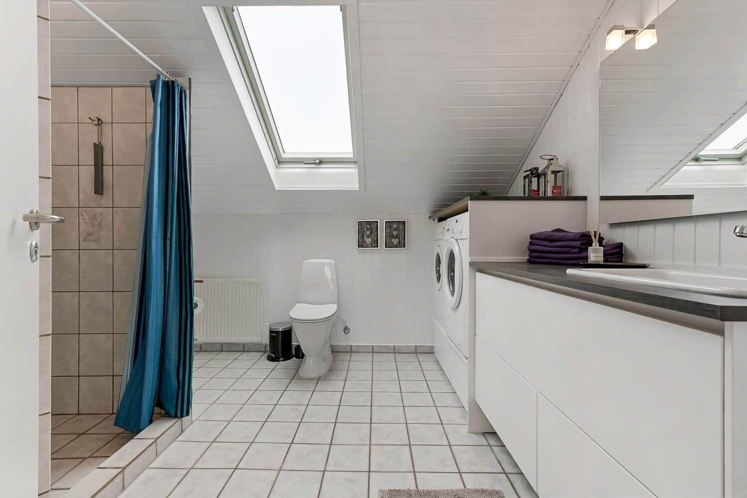 Badezimmer mit Dusche, Toilette und Waschmaschine unter Dachschrägen.