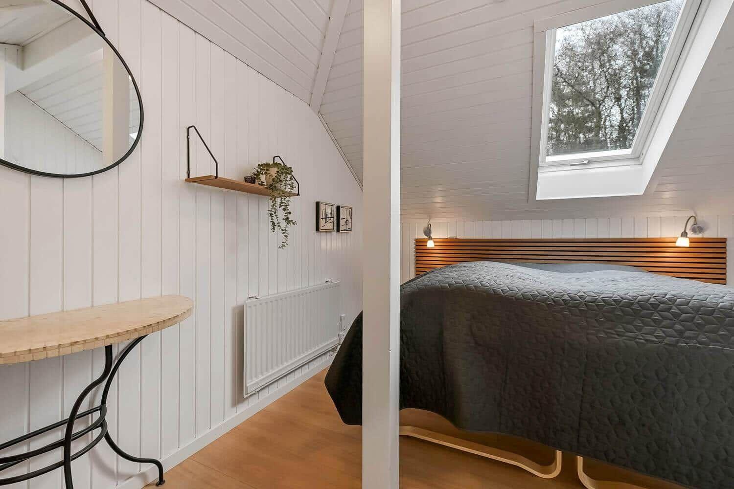 Schlafzimmer mit Dachfenster, Bett mit Holzrahmen und Wandspiegel.