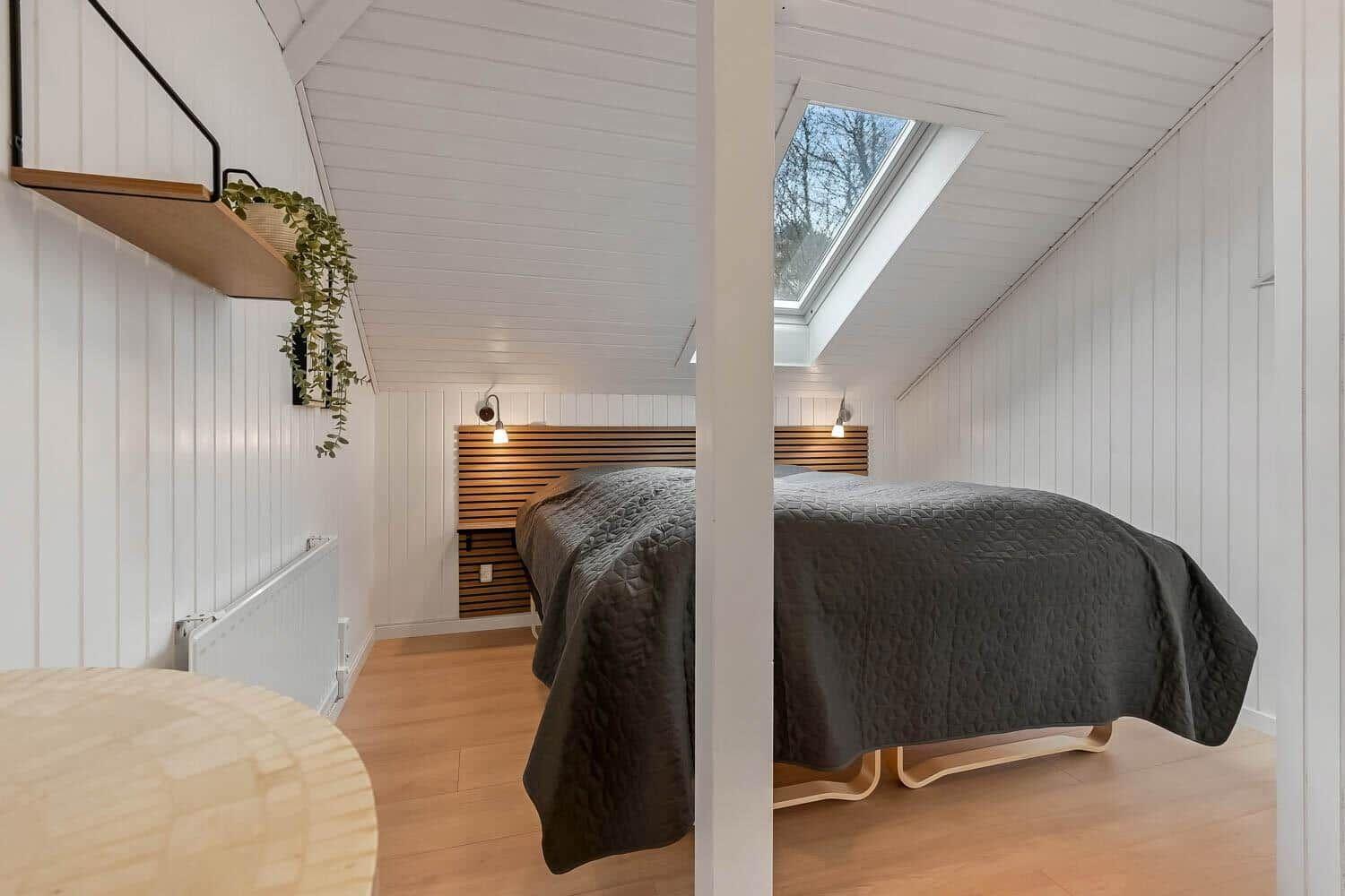 Schlafzimmer mit Dachfenster, Holzboden und Bett mit dunkler Bettwäsche.