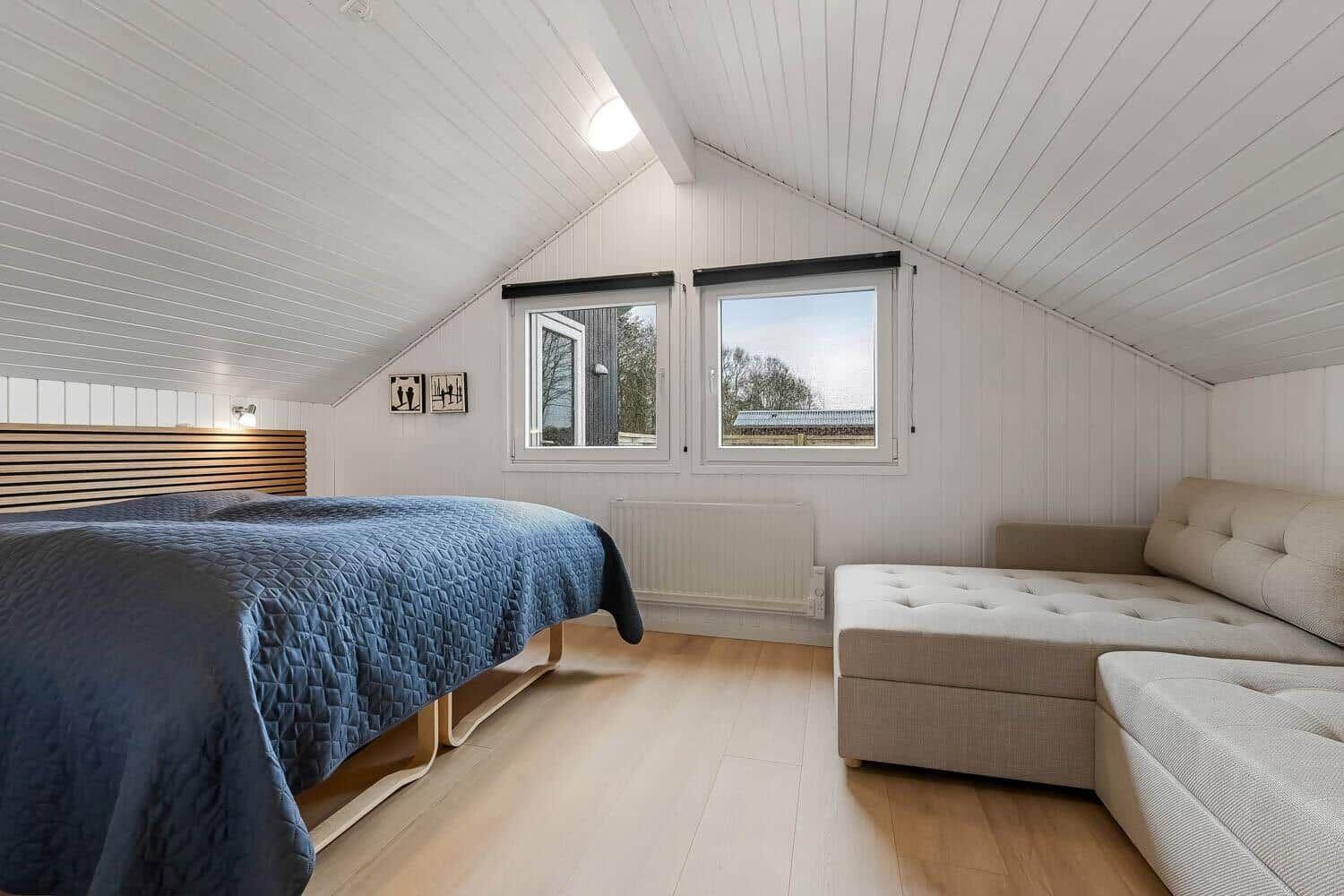 Schlafzimmer mit Bett, Sofa und zwei Fenstern an geneigtem Dach