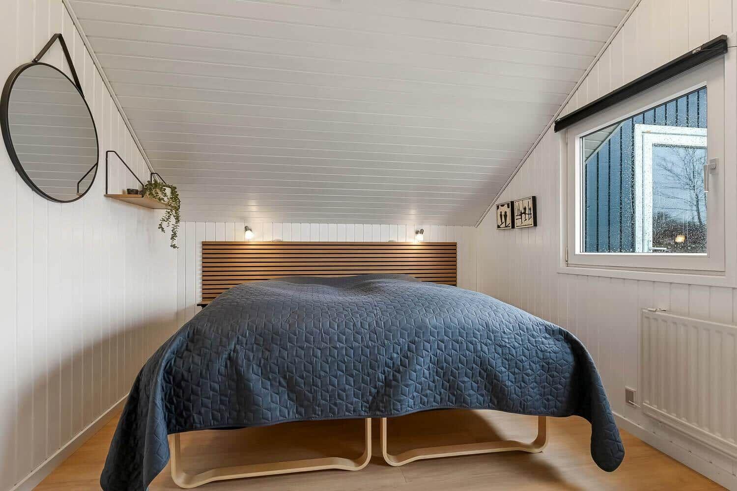 Schlafzimmer mit Bett, Fenster und Wandspiegel.