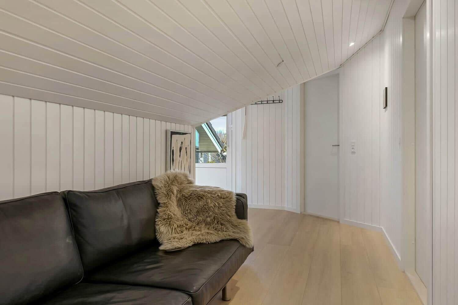 Schwarzes Sofa mit Felldecke, weiße Holzwände und Holzboden im Wohnbereich.