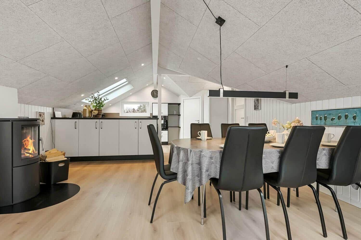 Esszimmer mit runder Tafel, schwarzen Stühlen und Kamin. Holzboden und schräges Dach mit Dachfenster.