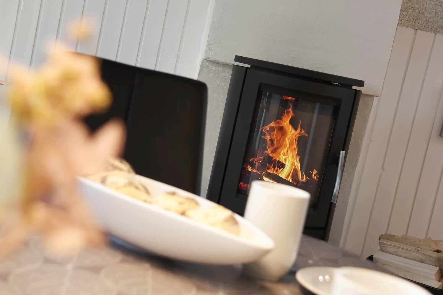 Ein Kamin mit brennendem Feuer und eine Tischplatte mit Tassen und Schale.