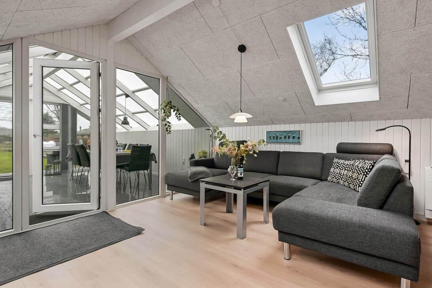 Wohnbereich mit grauem Sofa, Tisch und Fenstern zur Terrasse.