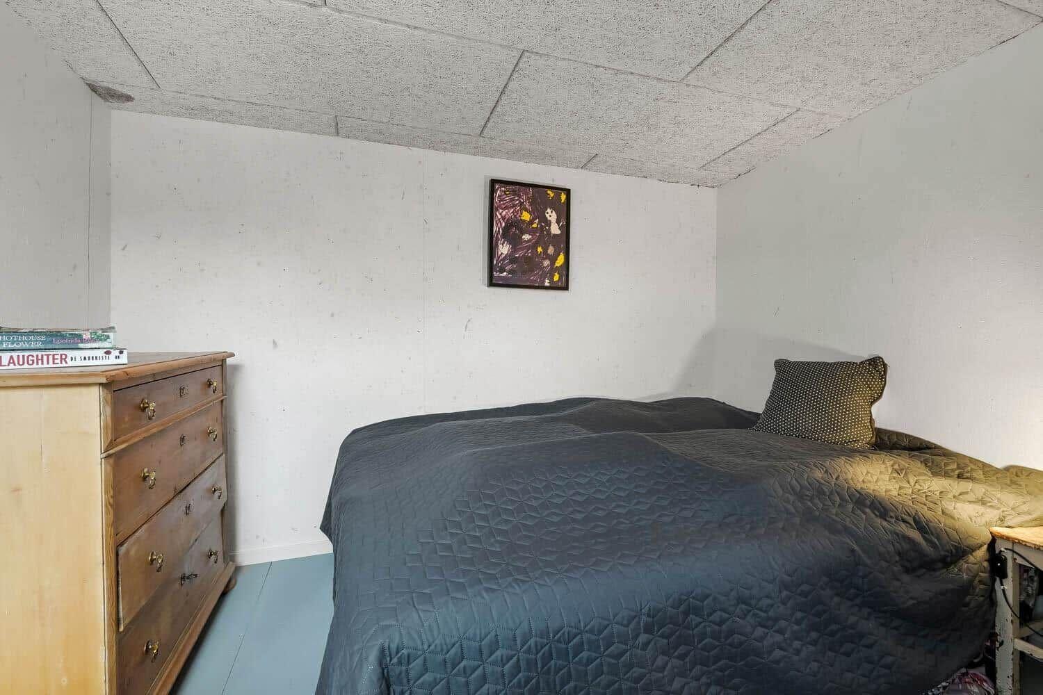 Schlafzimmer mit Bett, Holzkommode und Wandbild.