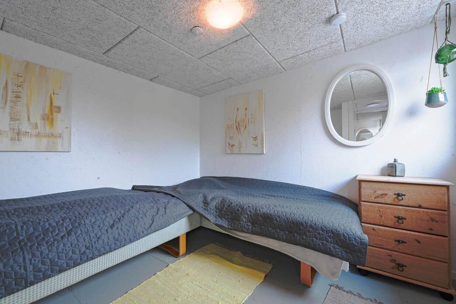 Zimmer mit zwei Betten, Holzkommode und runden Spiegel an der Wand.