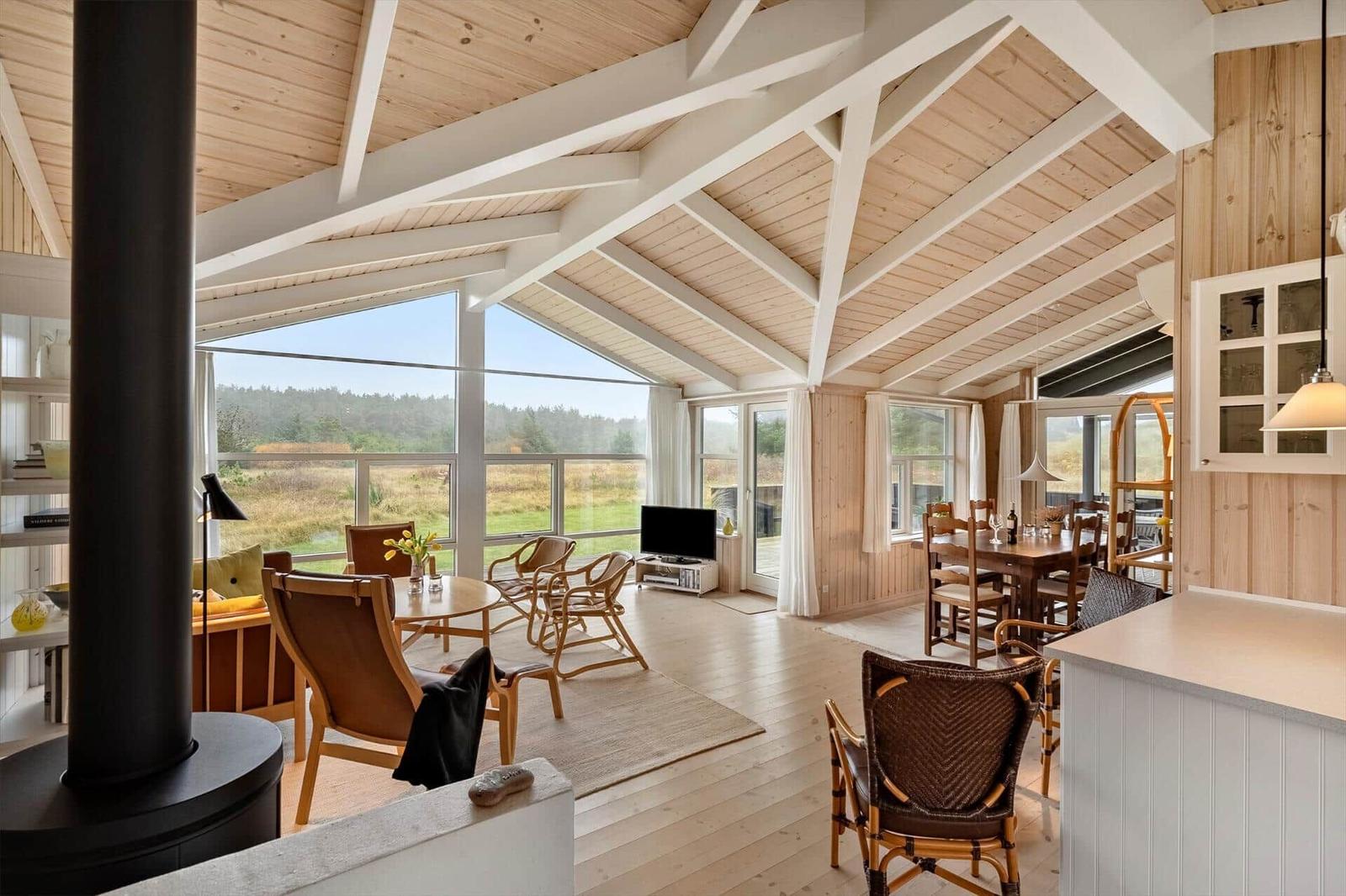 Großes Wohn- und Esszimmer mit Holzdecke und Blick auf Landschaft.