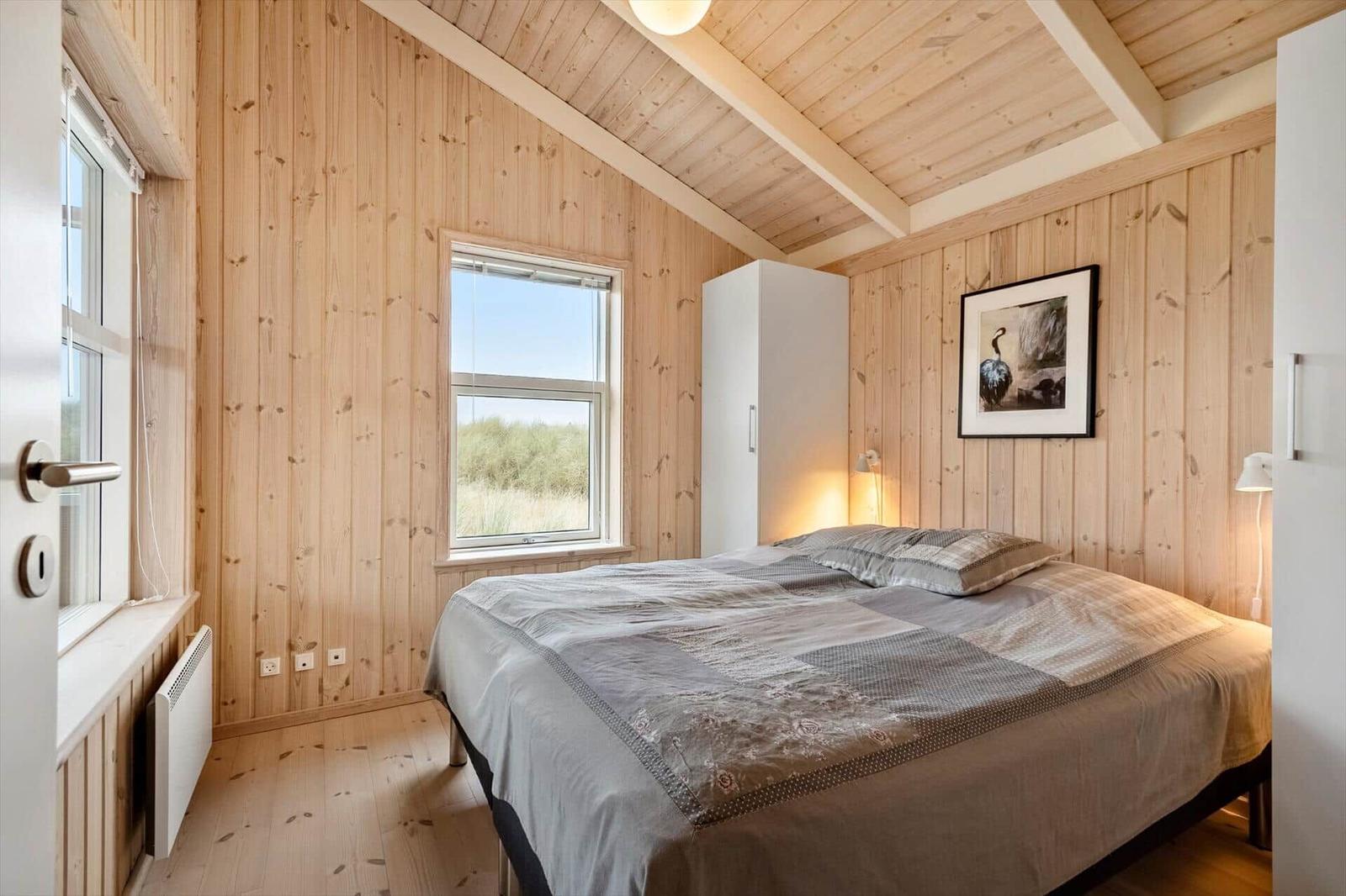 Schlafzimmer mit Holzwänden, Bett und Fenster zum Blick auf Grasland.