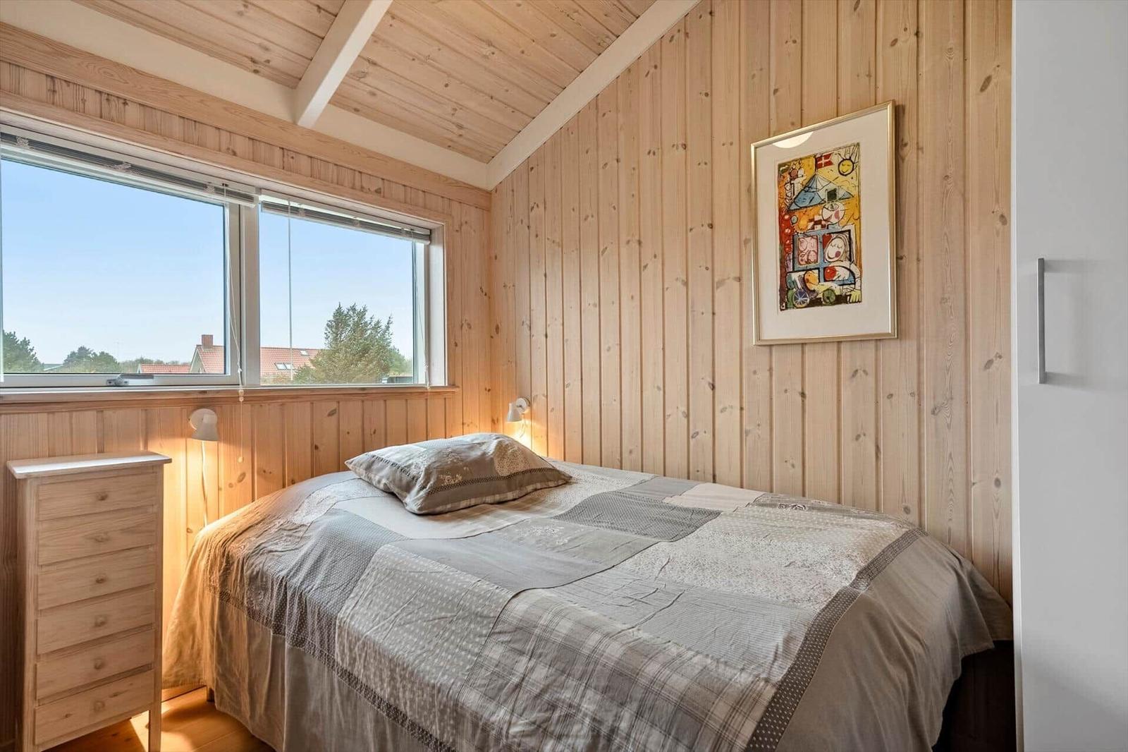 Schlafzimmer mit Holzwand, Bett, Schrank und Fenster.