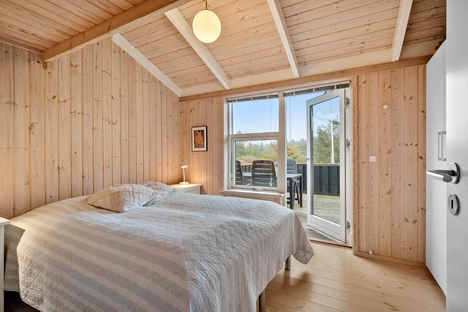 Schlafzimmer mit Holzwand, Bett und Balkonzugang.