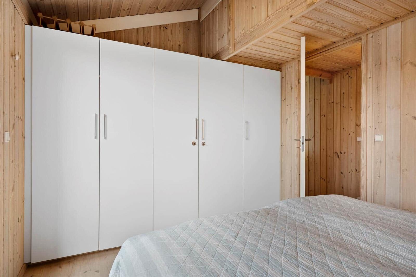 Schlafzimmer mit weißem Schrank und Holzwandverkleidung.