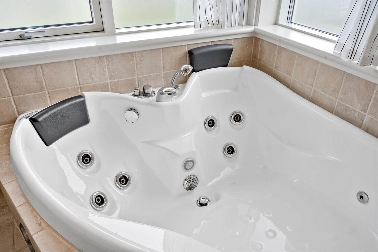 Eckbadewanne mit Duschkopf und mehreren Massagehöhlen.