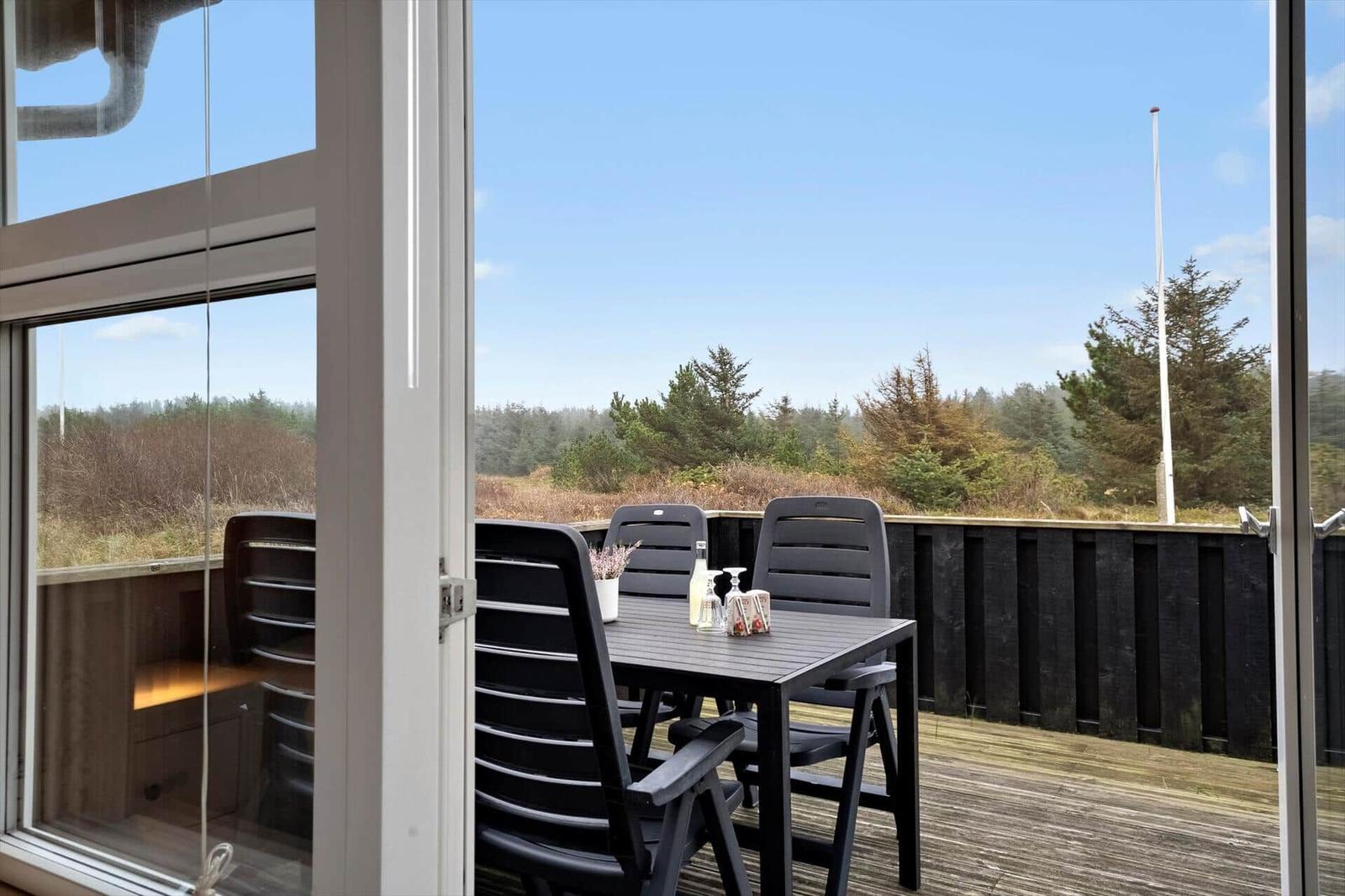 Terrasse mit Tisch und Stühlen, Blick auf Wald und Himmel.
