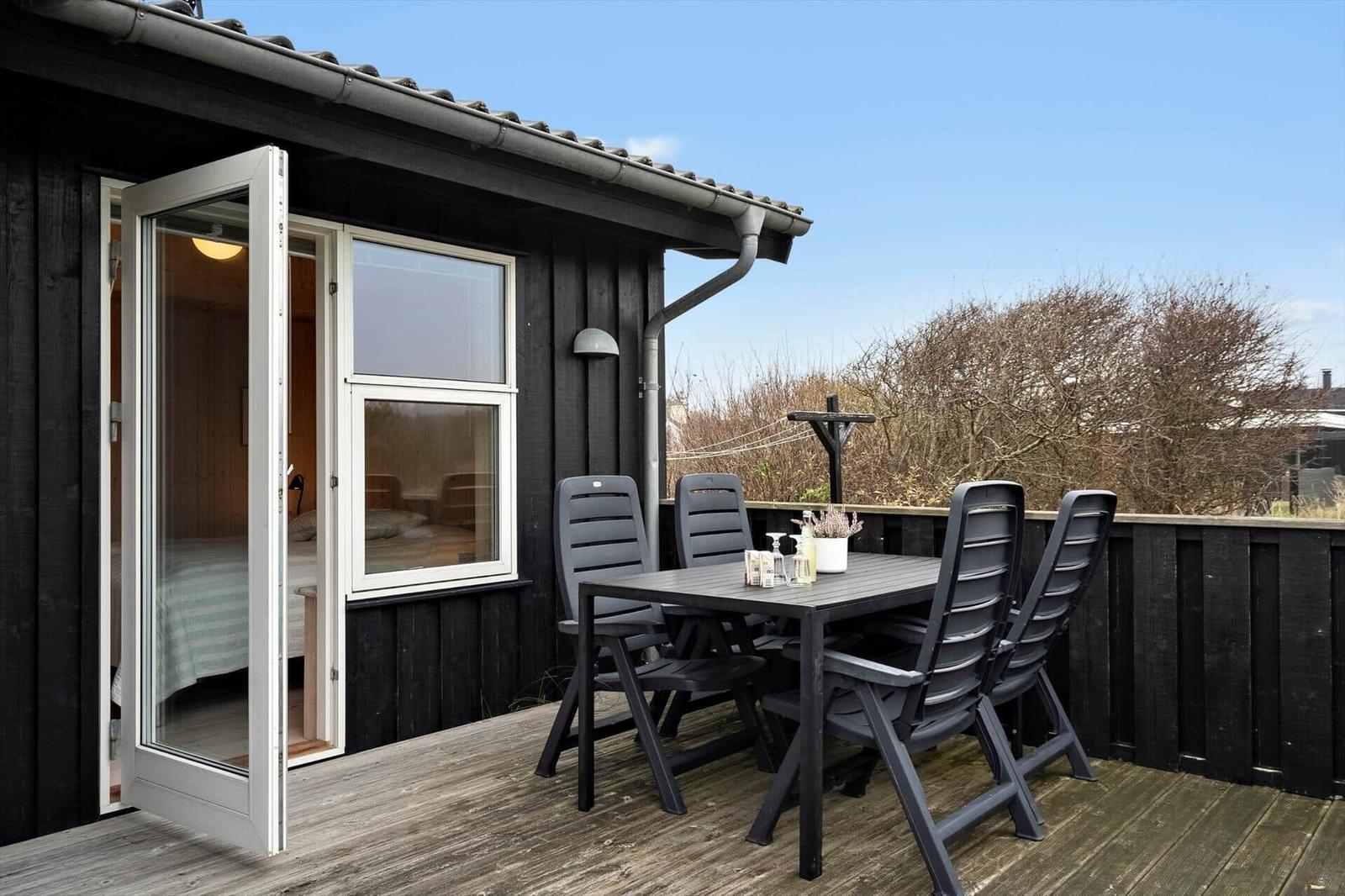 Terrasse mit Tisch und Stühlen neben einem Haus mit offener Tür.